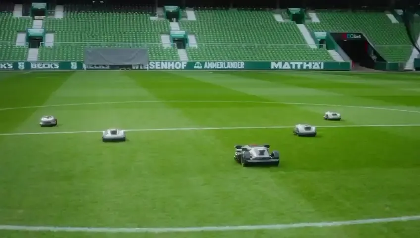 Mehrere Mähroboter mähen ein Fußballfeld in Bahnen